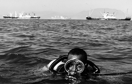 Scuba diver at the surface of the water with 3 large ships in the distace.