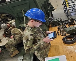A 91S Stryker Systems Maintainer student is using the Stryker tablet while pulling the 120mm motor assembly from a Stryker Motor Carrier Vehicle.